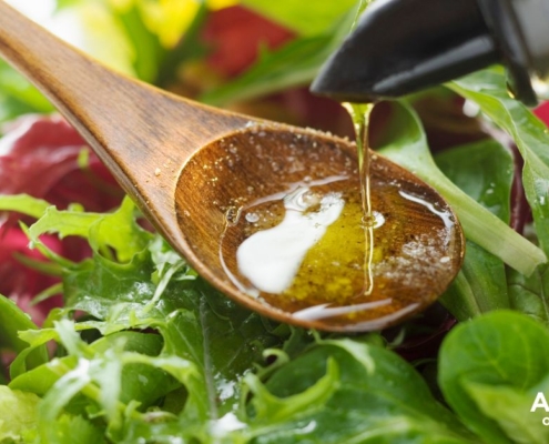person pouring oil into a spoon over a salad - Anytime Olive Oil Products olive oil pour spouts